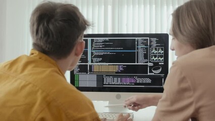 Over the shoulder shot of two male friends discussing program codes on black screen of computer monitor