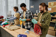 © pressmaster - Row of young intercultural people sorting second hand clothes for those in need while standing by table in office of volunteering organization