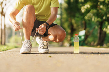 Wall Mural - Young athlete man tying running shoes with Energy Drink water, male runner ready for jogging outside, asian Fitness walking and exercise in the park morning. wellness, wellbeing and sport concepts