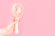 © TATIANA - Female hand holding a small fan on pink background close-up.
