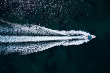 Wall Mural - Big white boat with a blue awning fast movement on dark water top view.