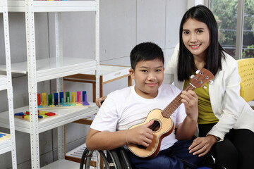 Wall Mural - Disabled kids classroom, happy schoolboy on wheelchair learning to play ukulele with teacher, student have fun together during study at school, kid education with physical disability and intellectual.