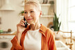 © Anatoliy Karlyuk - Happy mature lady with stylish short haircut having phone conversation standing at kitchen, talking to her beauty master, making an appointment for next week, listening attentively with smiling face