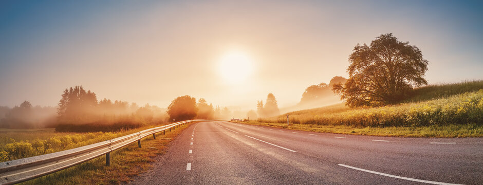 Fototapete - Sunrise in the foggy morning on the empty asphalt country winding road.
