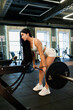 © dmshpak - A young sporty girl in the gym does exercises with a barbell. Athletic body. View from the back