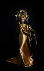  fantasy portrait of beautiful african woman model with afro, goddess silk robes and ornate floral wreath crown. gestural Posing holding golden flowers. isolated on dark  studio background 