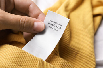 Poster - Woman holding clothing label on yellow garment, closeup