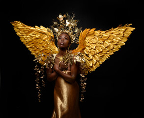 Wall Mural -  fantasy portrait of beautiful african woman model with afro, goddess silk robes, ornate crown & gold angel wings.  gestural Posing holding golden flowers., isolated on dark  studio background 