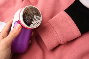 Canvas Print - Woman holding fabric shaver near sweater with lint, closeup