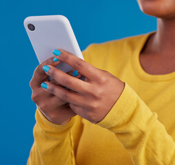 Wall Mural - Phone, typing and closeup of hands of woman in studio for social media, text message and browse website. Communication, technology and girl on internet, network and chat online on blue background