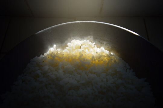 a ray of sunlight illuminates the end of an old iron skillet filled with rice in an unlit place. con