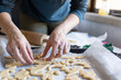 © KONSTANTIN SHISHKIN - Baking cookies - a woman lays out the dough in the shape of dinosaurs on a baking sheet