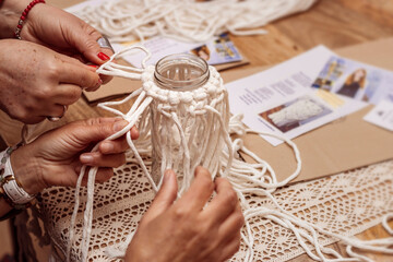 White macrame. Close-up of the hands of two elderly women tying macrame knots.