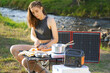 Woman uses solar panel and power station outdoors on camping to generate electricity for cooking