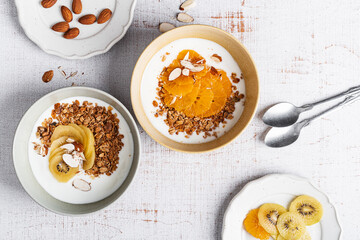 Wall Mural - Bowls of yogurt with granola, kiwi, and orange fruits,  top view. Healthy  breakfast