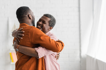 carefree african american man hugging adult son at home.