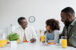 © LIGHTFIELD STUDIOS - happy middle aged man looking at african american granddaughter near son during family breakfast.