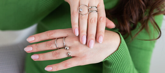 Wall Mural - Banner close up female hands with trendy light pink manicure wear stylish rings jewelry. Silver ring and accessory bijouterie concept