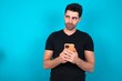 © Jihan - Young man wearing black T-shirt over blue studio background holds telephone hands reads good youth news look empty space advert