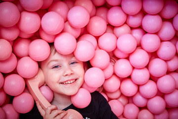 A cheerful girl with a retro handset in her hands lies in the pink balls of a dry pool.