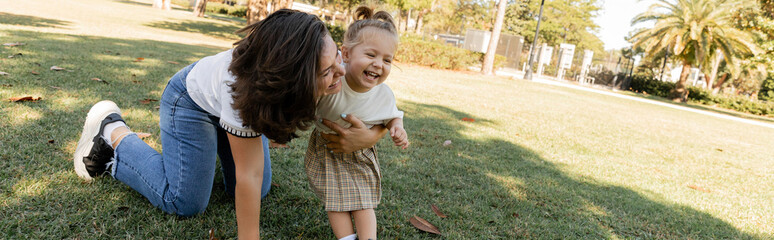 toddler girl laughing with happy mother while playing together in Miami park, banner.