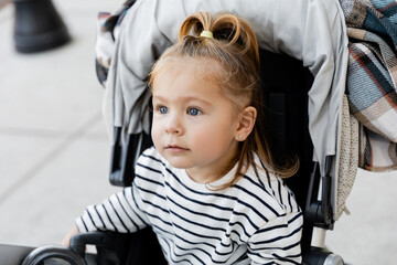 toddler girl in striped long sleeve shirt sitting in baby stroller.