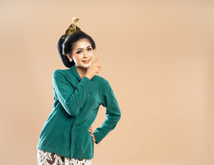 Wall Mural - smiling asian woman in green kebaya looking and pointing on her left side while put her hand on her waist on isolated bacground