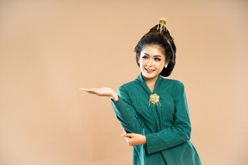 Wall Mural - javanese woman in green kebaya standing and pointing on her right side on isolated background