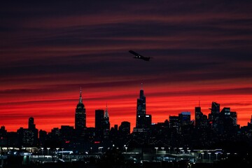 Wall Mural - Beautiful view of a plane flying over the night skylines of NYC on a sunset sky background