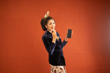 Wall Mural - javanese woman in bludru kebaya standing with smile while showing the blank phone on isolated background