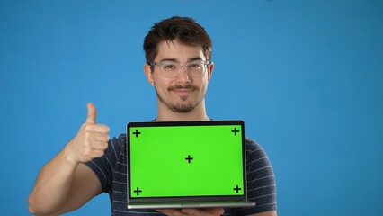 Wall Mural - Young smiling happy man 20s wear striped t-shirt hold use laptop pc computer with tracking points green screen, browsing chatting with blank screen workspace area isolated on solid blue background
