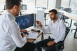 © Serhii - Two successful trader sitting in office and looking at screen, checking cryptocurrency information data on finance market graph, pointing on monitor