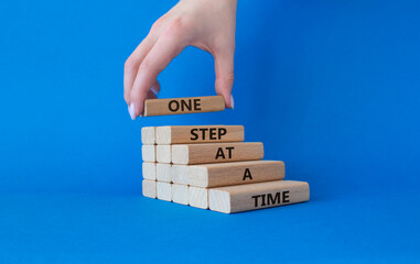 Wall Mural - One step at a time symbol. Concept words One step at a time on wooden blocks. Beautiful blue background. Businessman hand. Business and One step at a time concept. Copy space.