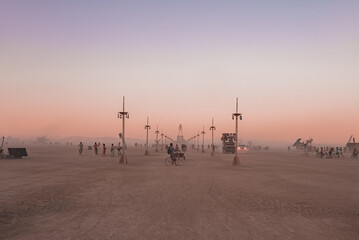 People walking towards sunset at a festival in the desert. Beautiful music festival in a desert at the Burning Man festival. Main entrance to the statue of a man.