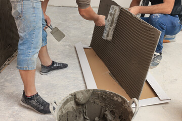 Sticker - Worker spreading adhesive mix over tile with spatula, closeup