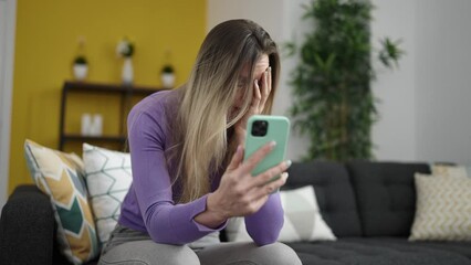 Poster - Young blonde woman using smartphone sitting on sofa at home