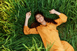 © VICHIZH - a joyful woman in a long orange dress lies in the tall green grass and looking at the camera smiles broadly