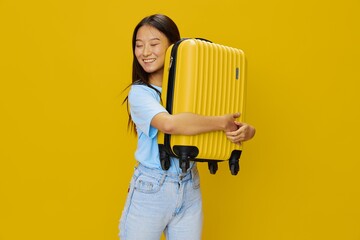 Wall Mural - Asian woman traveling with yellow suitcase and tickets with passport in hand, tourist traveling by plane and train with luggage on yellow background in blue T-shirt and jeans