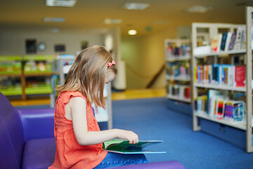 Wall Mural - Preschooler old girl reading a book in municipal library