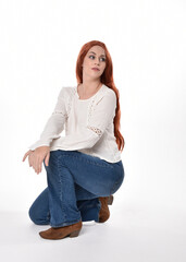 Canvas Print - full length portrait of beautiful woman model with long red hair, wearing casual outfit white blouse  top and denim jeans, isolated on white studio background. Relaxed seated pose, sitting on floor wi