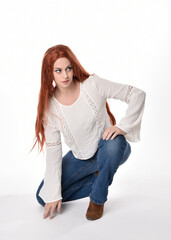 Canvas Print - full length portrait of beautiful woman model with long red hair, wearing casual outfit white blouse  top and denim jeans, isolated on white studio background. Relaxed seated pose, sitting on floor wi