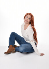 Canvas Print - full length portrait of beautiful woman model with long red hair, wearing casual outfit white blouse  top and denim jeans, isolated on white studio background. Relaxed seated pose, sitting on floor wi