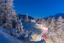 Car Trails Lights On Snowy Mountain Road Leading To Chiesa Bianca Under The Stars, Maloja, Engadine, Canton Of Graubunden, Switzerland