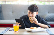 Asian man in black shirt looking at digital tablet while comfortably setting on floor in living room., happy relaxing man watch movies online and internet browsing social media during eating croissant