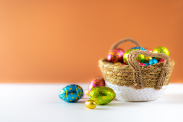 Wall Mural - Easter eggs in basket with cream background on white table. Studio lighting colorful easter decorated eggs for egg hunt with wicker basket and flowers. Banner for web and composition. Wishes card