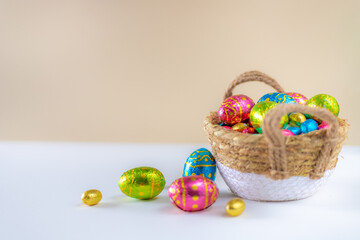 Wall Mural - Easter eggs in basket with cream background on white table. Studio lighting colorful easter decorated eggs for egg hunt with wicker basket and flowers. Banner for web and composition. Wishes card