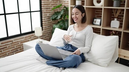 Wall Mural - Young beautiful hispanic woman having video call sitting on bed at bedroom