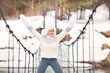 Outdoor portrait of happy woman raised her hands up, enjoys and fun on suspension bridge in winter