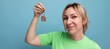 close-up of lucky cute blond woman in casual look holding apartment keychain on blue background