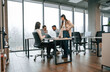 © standret - Against big windows by the table. Four people are working in the office together